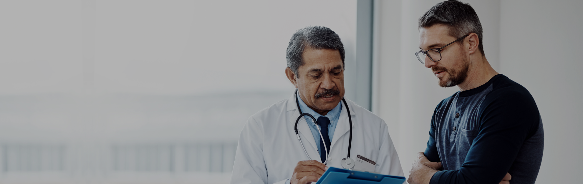 Man and male doctor looking down at clipboard in doctor's hands.