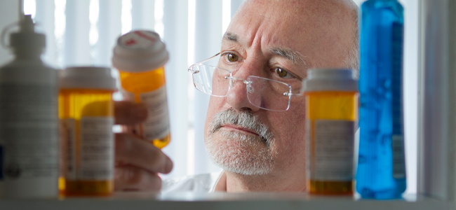 Older man with glasses looking at pill bottle.